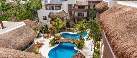 A resort with multiple buildings, a central swimming pool, and thatched-roof structures.