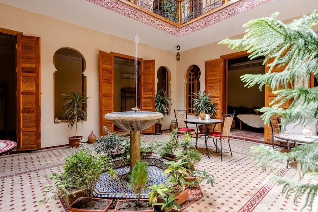 Un patio con una fuente, plantas en macetas y un área de comedor con sillas y una mesa.