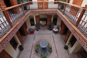 A courtyard with a fountain, tiled floor, and a seating area with chairs and tables.