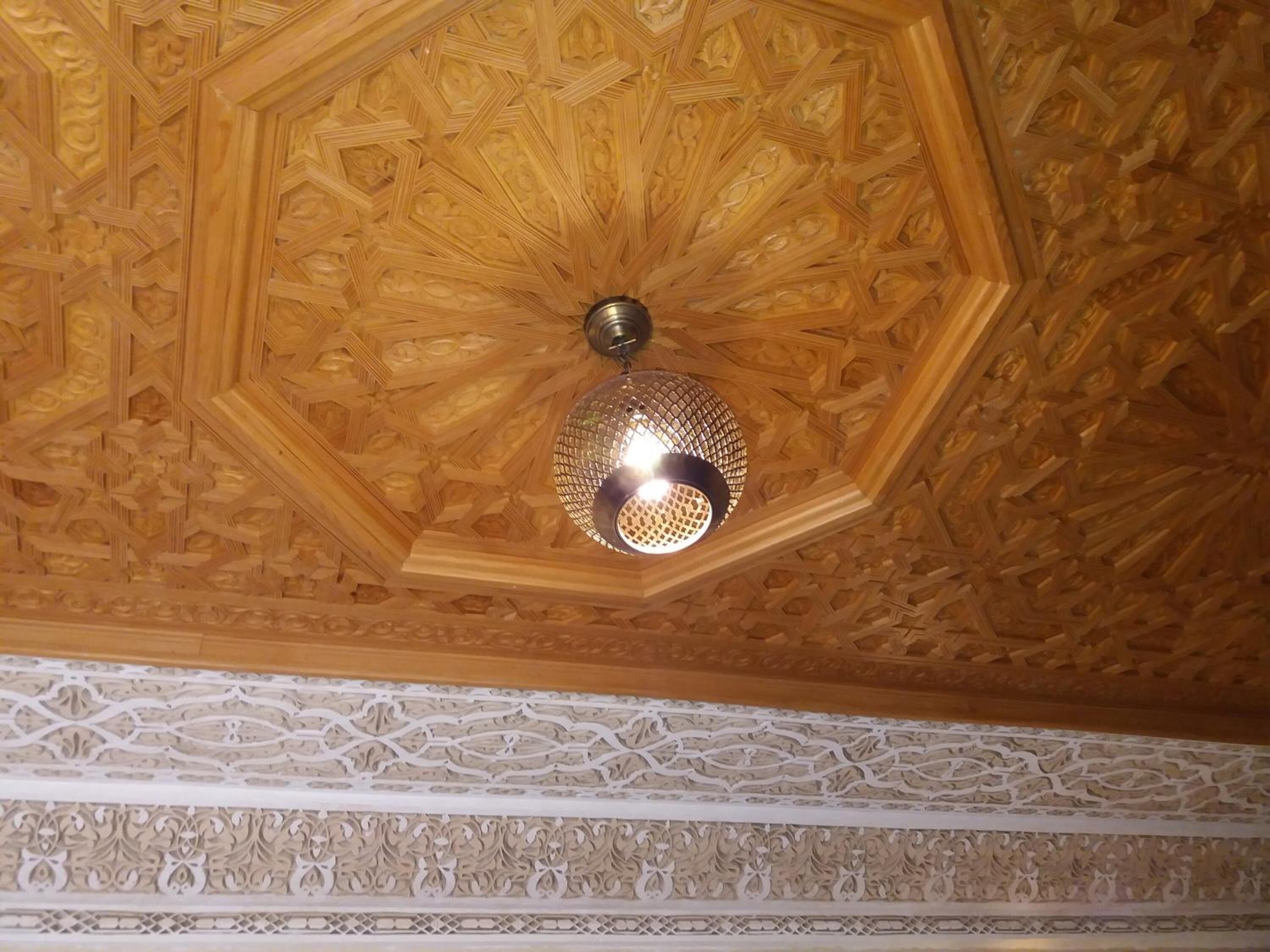 A ceiling with intricate geometric patterns and a hanging spherical light fixture.