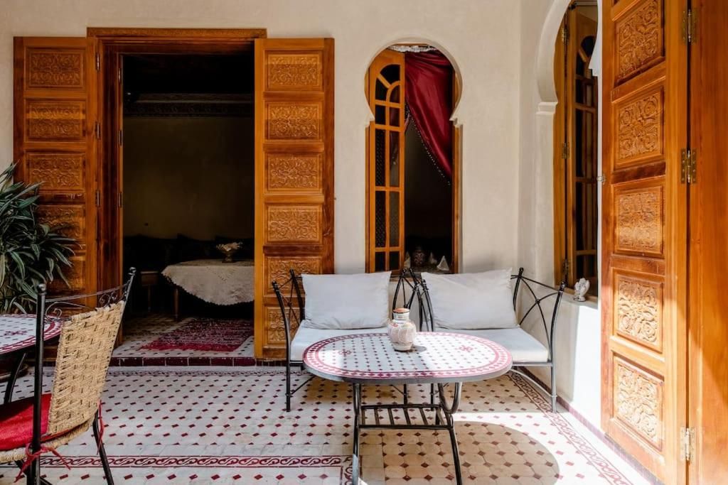 Un umbral abierto que da a una habitación con una cama, una mesa y una silla, y un suelo con diseño.