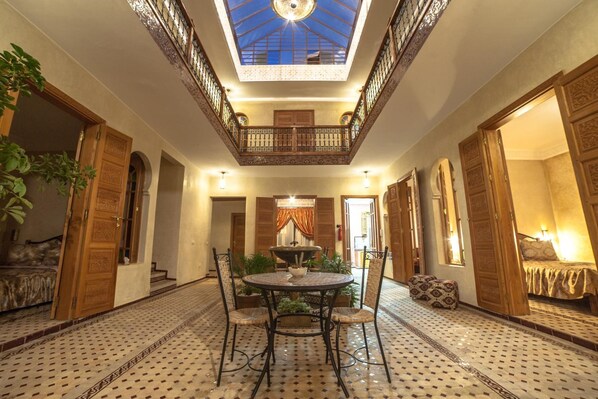 A spacious room with a high ceiling, a central round table, and a balcony with ornate railings.