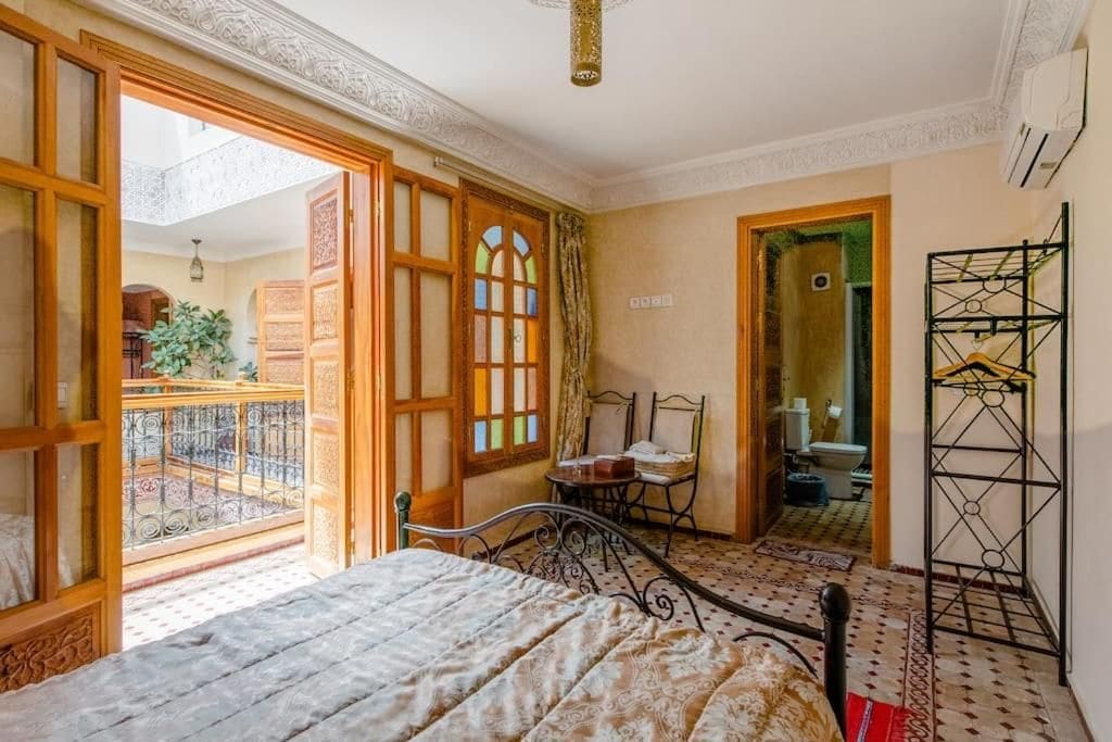 A room with a bed, a chair, a small table, and a balcony.