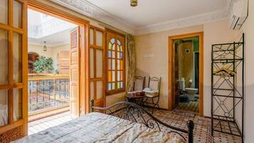 A room with a bed, a chair, a small table, and a balcony.