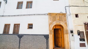 A building with a large wooden door, a stone wall, and a window with a metal grille. - Riad Dar Saidi (Rabat)