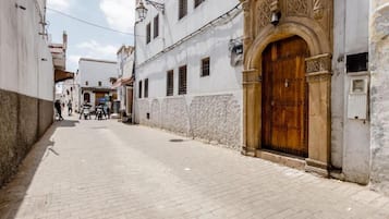 Uma rua estreita com uma porta de madeira destacada e uma placa em cima.