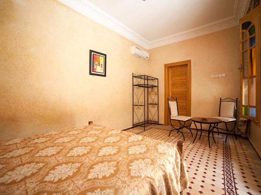 A room with a bed, a small table with chairs, a radiator, and a door.