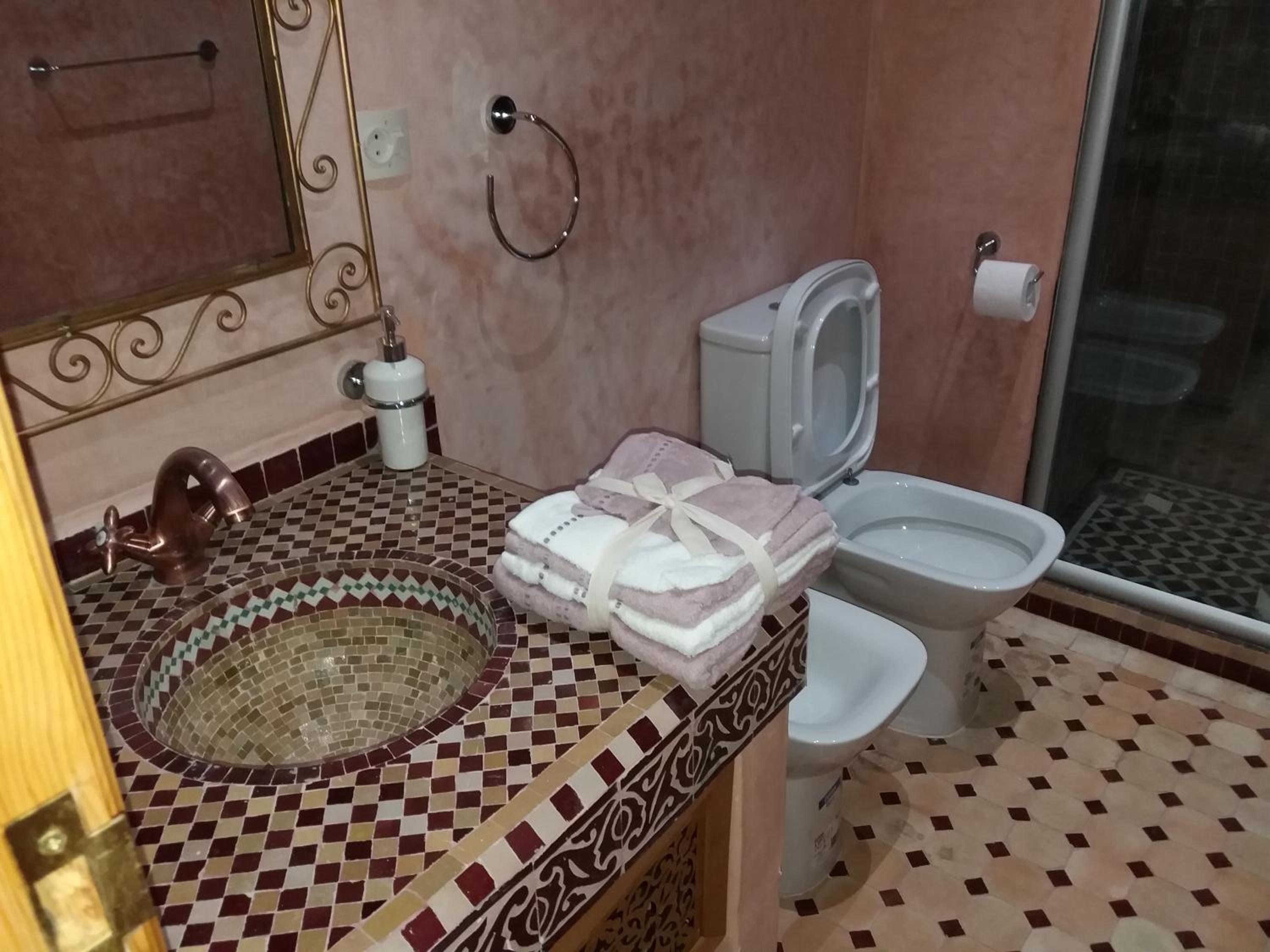 Un baño con suelo de mosaico, un lavabo con una pileta decorativa, un inodoro y una zona de ducha.