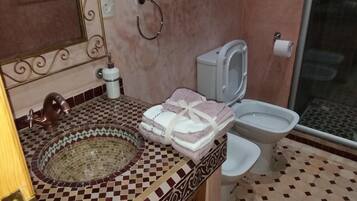 Un baño con suelo de mosaico, un lavabo con una pileta decorativa, un inodoro y una zona de ducha.