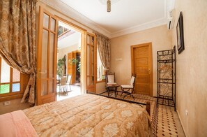A bedroom with a bed, a chair, a small table, and a door leading to a balcony.