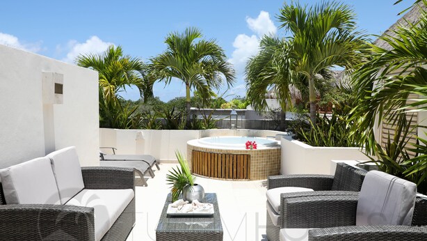 An outdoor patio area with wicker furniture, a hot tub, and tropical plants. - Turquesa Penthouse 2 BDRM sleeps 5 (Tulum)