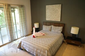 A hotel room with a large bed, two bedside tables with lamps, a window with curtains, and a wall-mounted abstract painting.