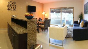 Cozinha moderna com bancadas de granito, sala de jantar com mesa de vidro e sala de estar com sofá e televisão.