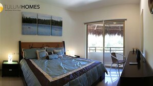 Quarto com cama grande, escrivaninha, cadeira, mesa de cabeceira e janela com vista para o exterior.