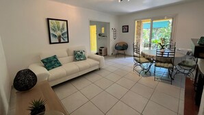 Una sala de estar con un sofá blanco, una mesa de comedor con sillas y una zona de cocina con estufa.