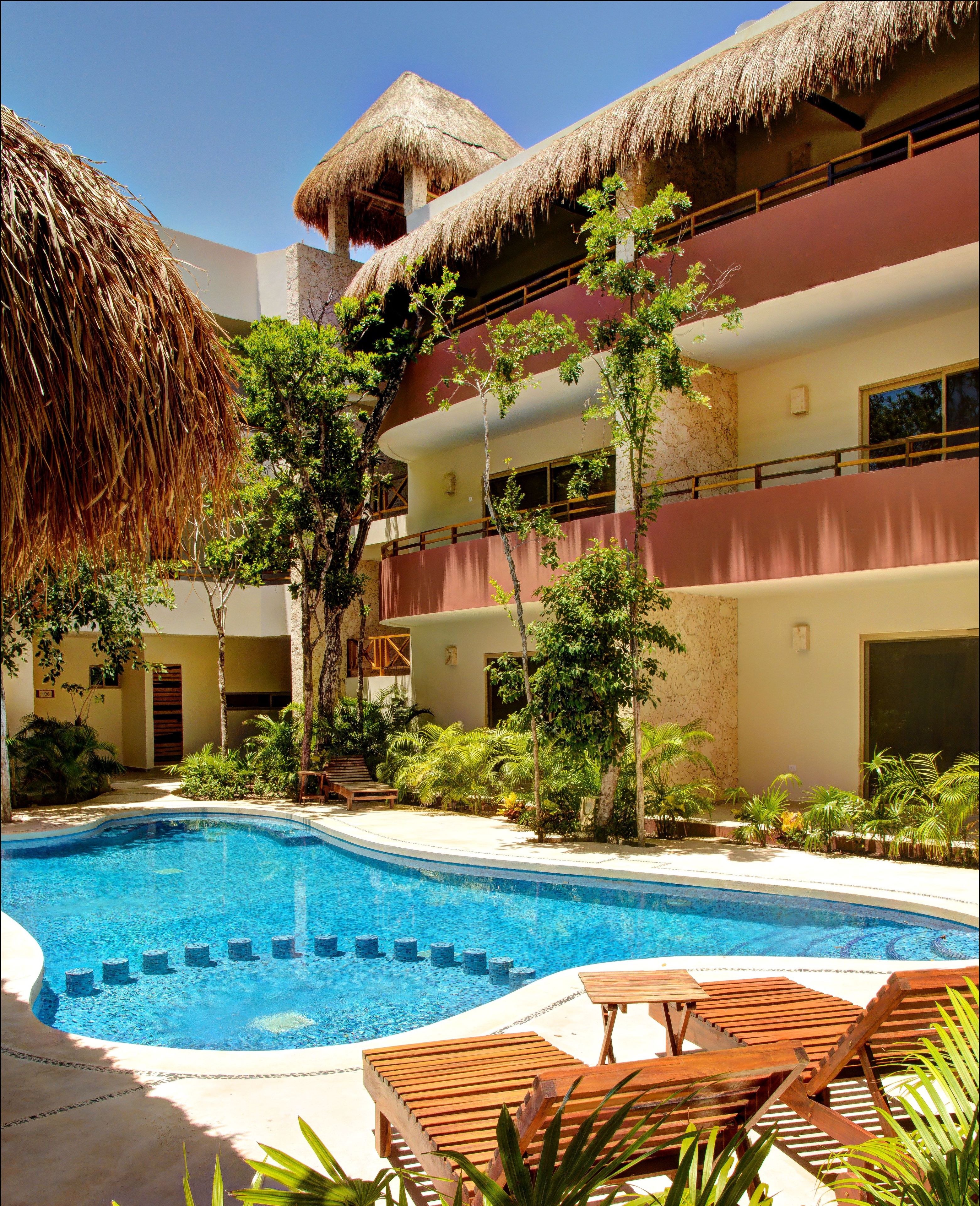 A hotel with a swimming pool, wooden lounge chairs, and a thatched-roof building.