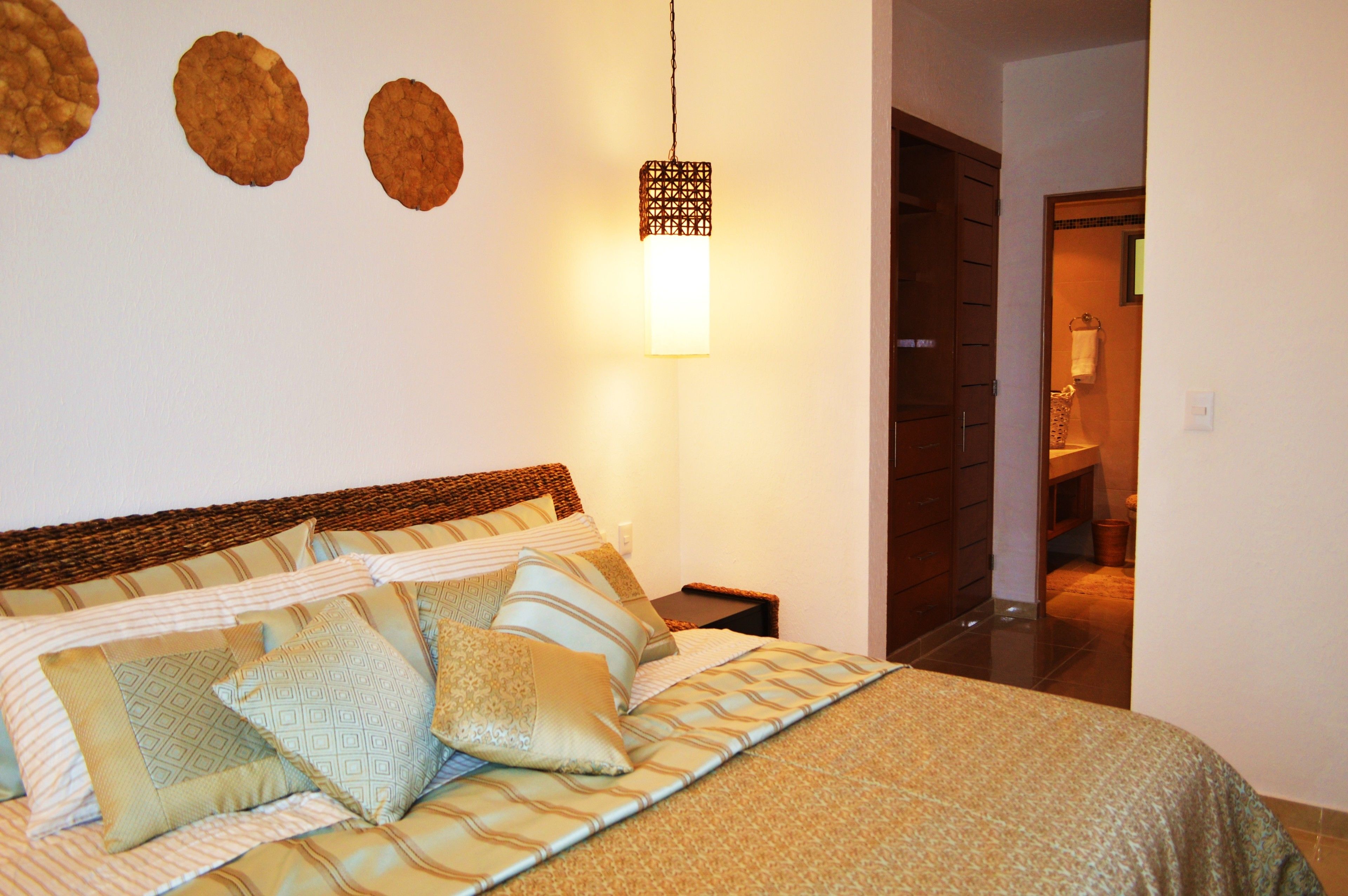A neatly made bed with patterned bedding and pillows, a hanging light fixture, and a wooden door in the background.