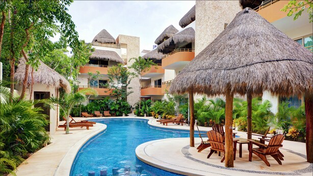 Een zwembadgedeelte van een resort, met rieten parasols, ligbedden en een centraal gelegen zwembad.