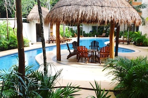 A pool area with a thatched umbrella, wooden chairs, and lounge chairs around the pool.