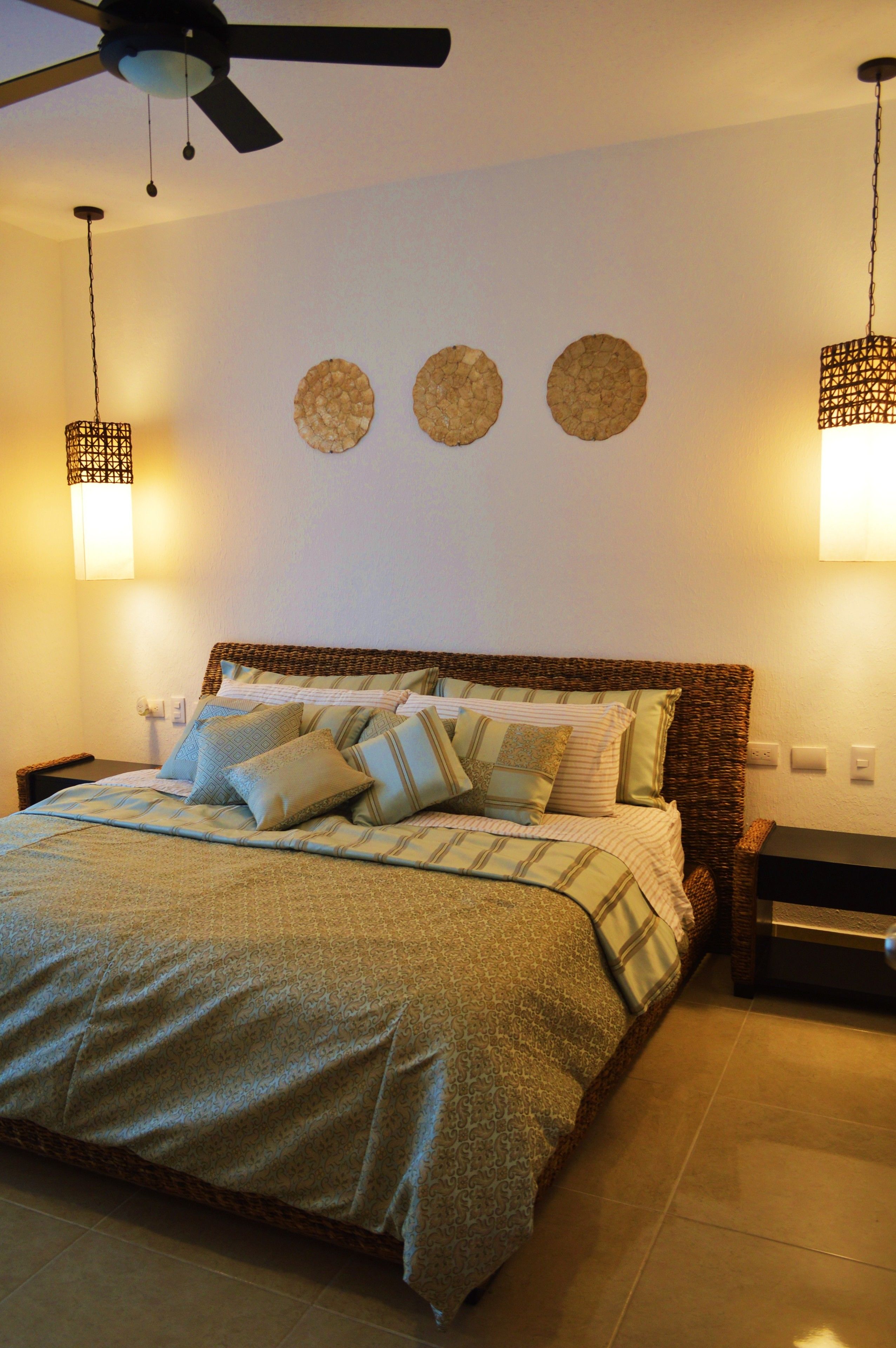 A neatly made bed with a patterned bedspread and pillows, a ceiling fan, and wall-mounted lamps.