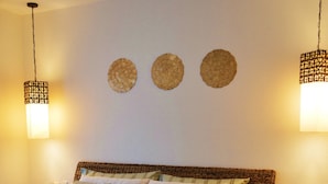Een keurig opgemaakt bed met een bedspreide en kussens, een plafondventilator en wandlampen.