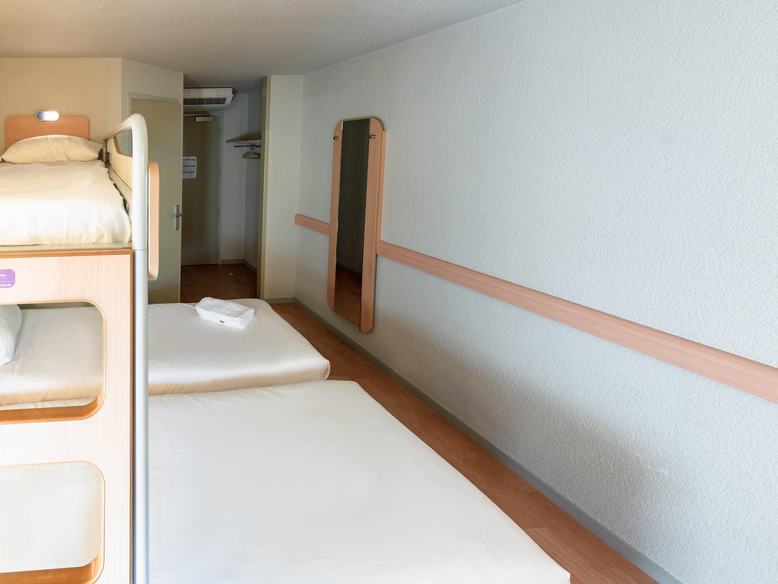 A compact hotel room with bunk beds, a small bathroom, and a mirror.