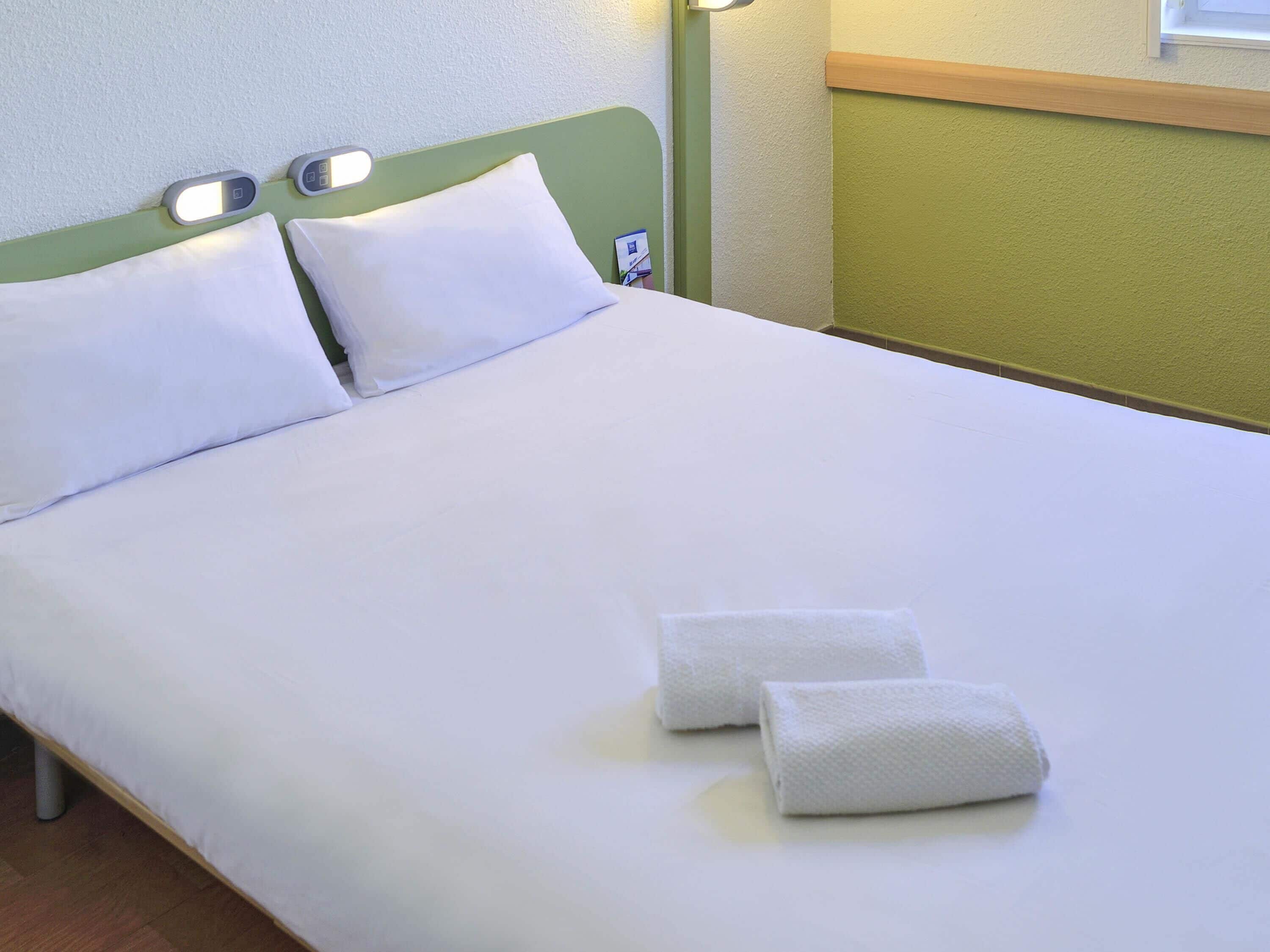 A neatly made bed with white linens and two towels folded at the foot.