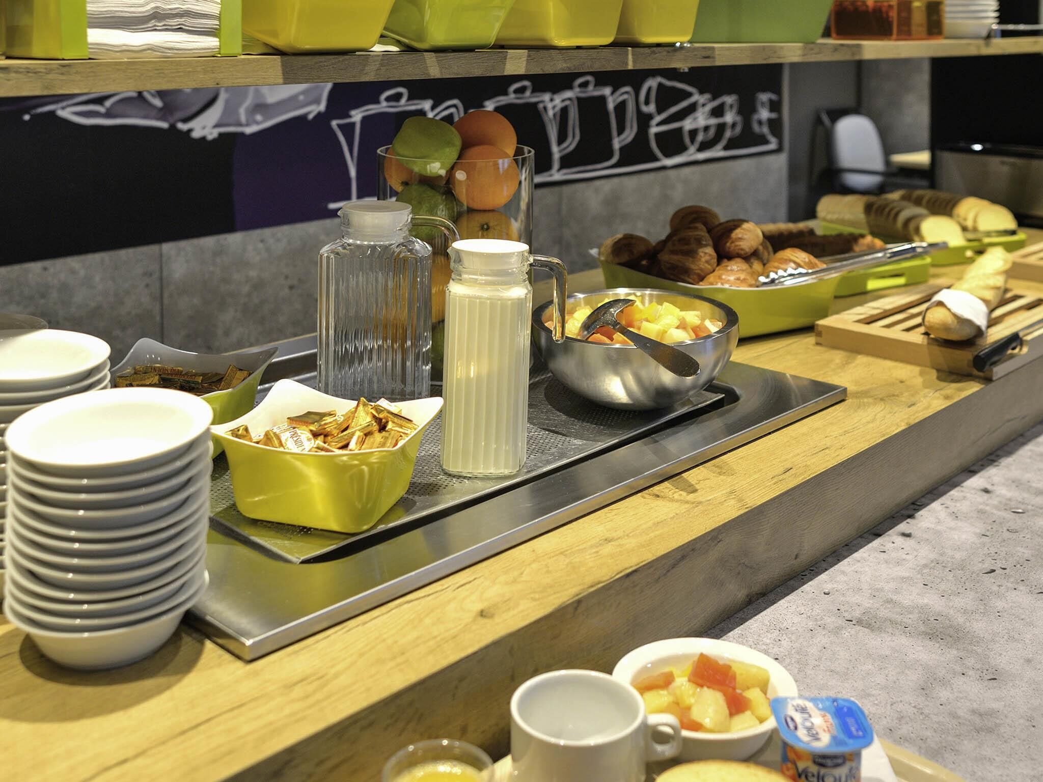 A breakfast buffet with various food items, a coffee machine, and stacked plates.