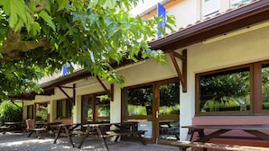An outdoor seating area with picnic tables and benches, surrounded by large windows and covered by a roof structure. - ibis budget Avignon Nord Le Pontet (Le Pontet)
