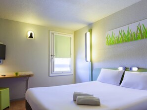 A hotel room with a bed, a bedside table, a wall-mounted TV, a window, and a painting of grass. - ibis budget Avignon Nord Le Pontet (Le Pontet)