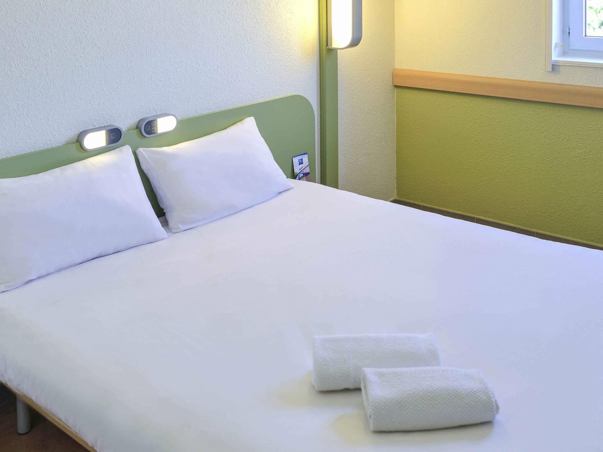 Un letto con lenzuola bianche, due cuscini e due asciugamani piegati.