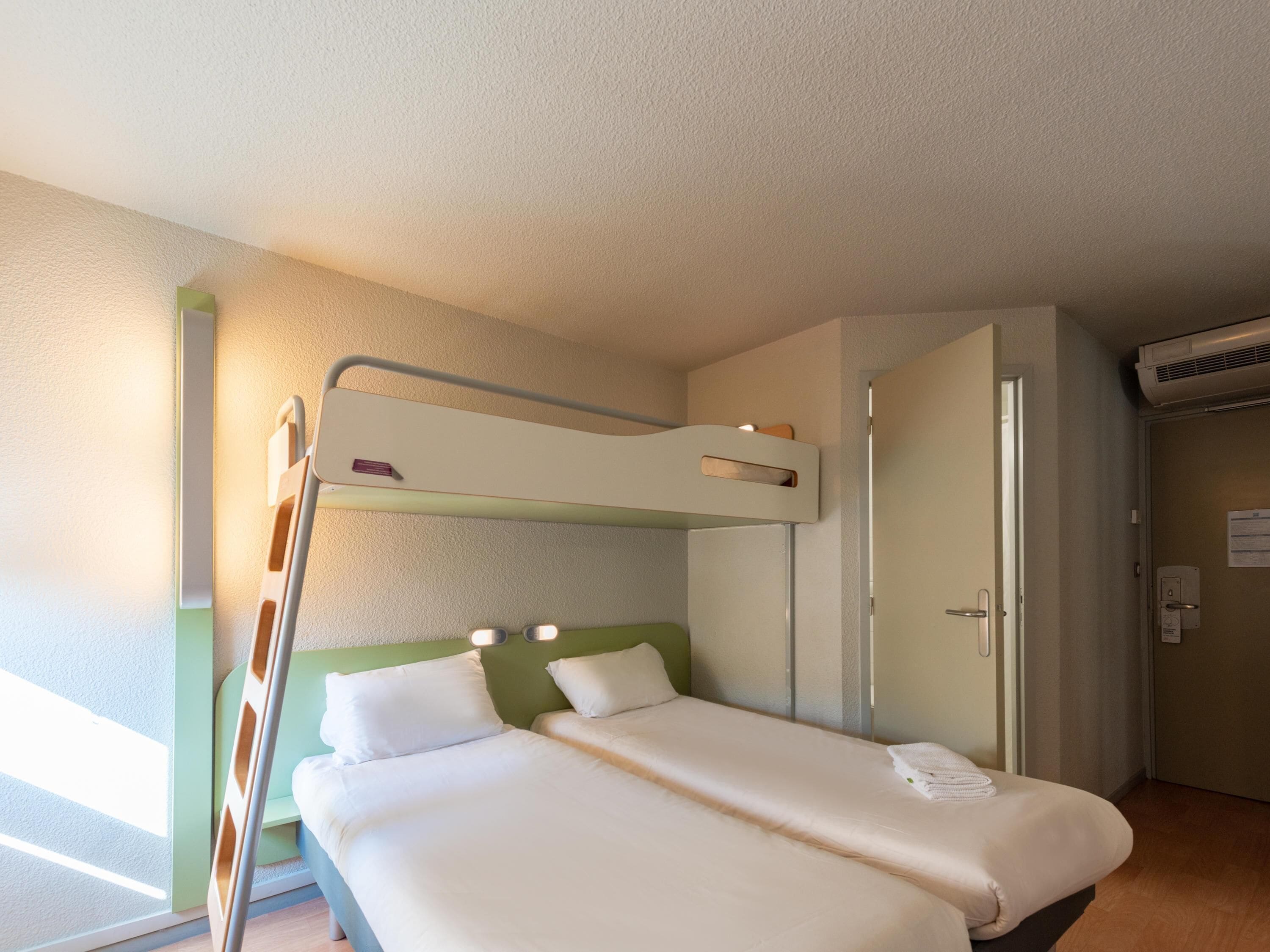A bunk bed with a ladder, a wardrobe, and an air conditioning unit in a room.