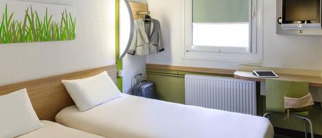 Una habitación de hotel con dos camas, un escritorio con una computadora, una ventana y un radiador.