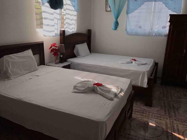 Habitación de hotel con dos camas, cada una con ropa blanca y un arreglo floral rojo.