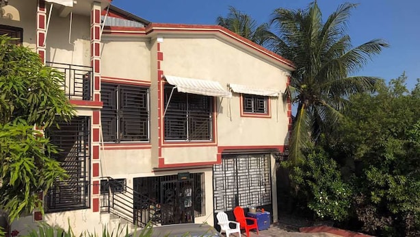 A two-story house with a balcony, a car parked in front, and a red chair outside. - Marcie Guesthouse hôtel and restaurant (Tabarre)