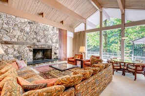 A spacious living area with a stone fireplace, comfortable seating, and large windows offering a view of the outdoors. - Exclusive House On Foothill with hot tub, sauna and jacuzzi. (Welches)