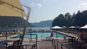 A poolside area with a view of a lake and mountains, outdoor seating, and umbrellas.