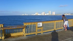 En träbrygga med utsikt över havet och en stadsbild i bakgrunden.