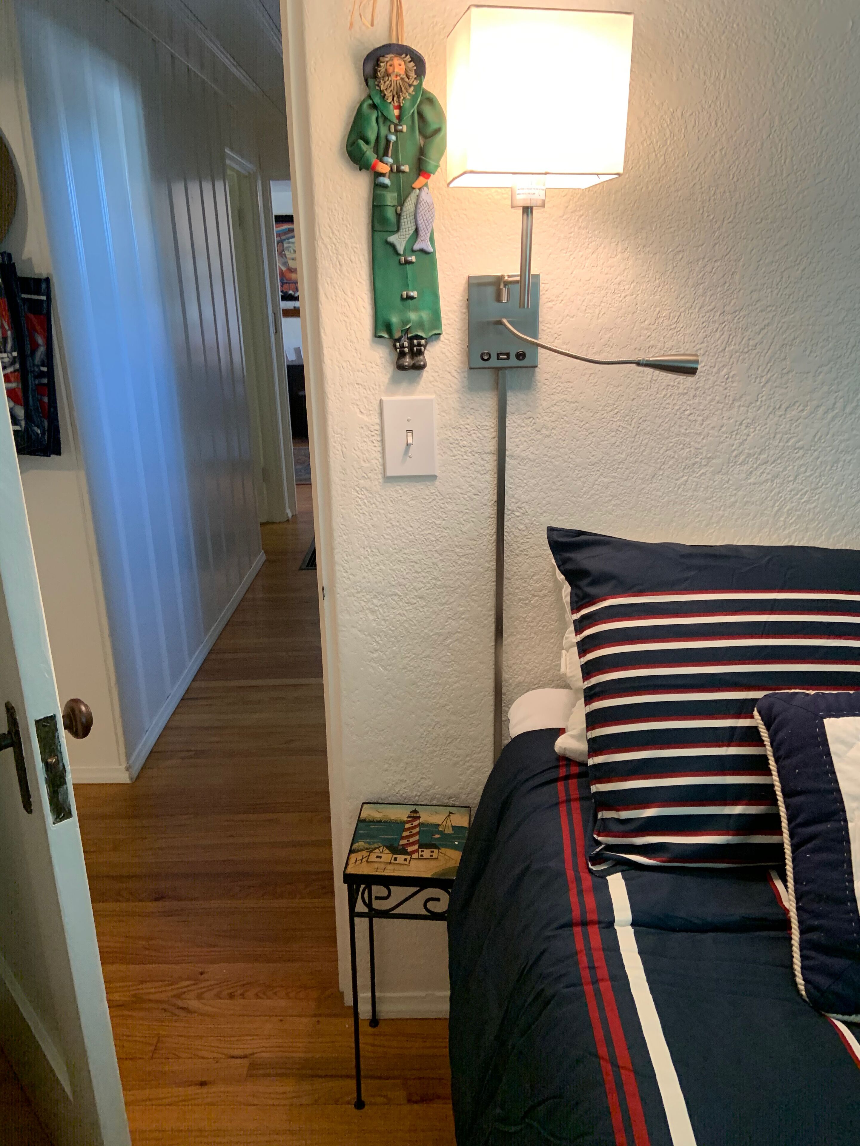 A bedroom with a bed, a nightstand, a lamp, a wall-mounted heater, and a door.