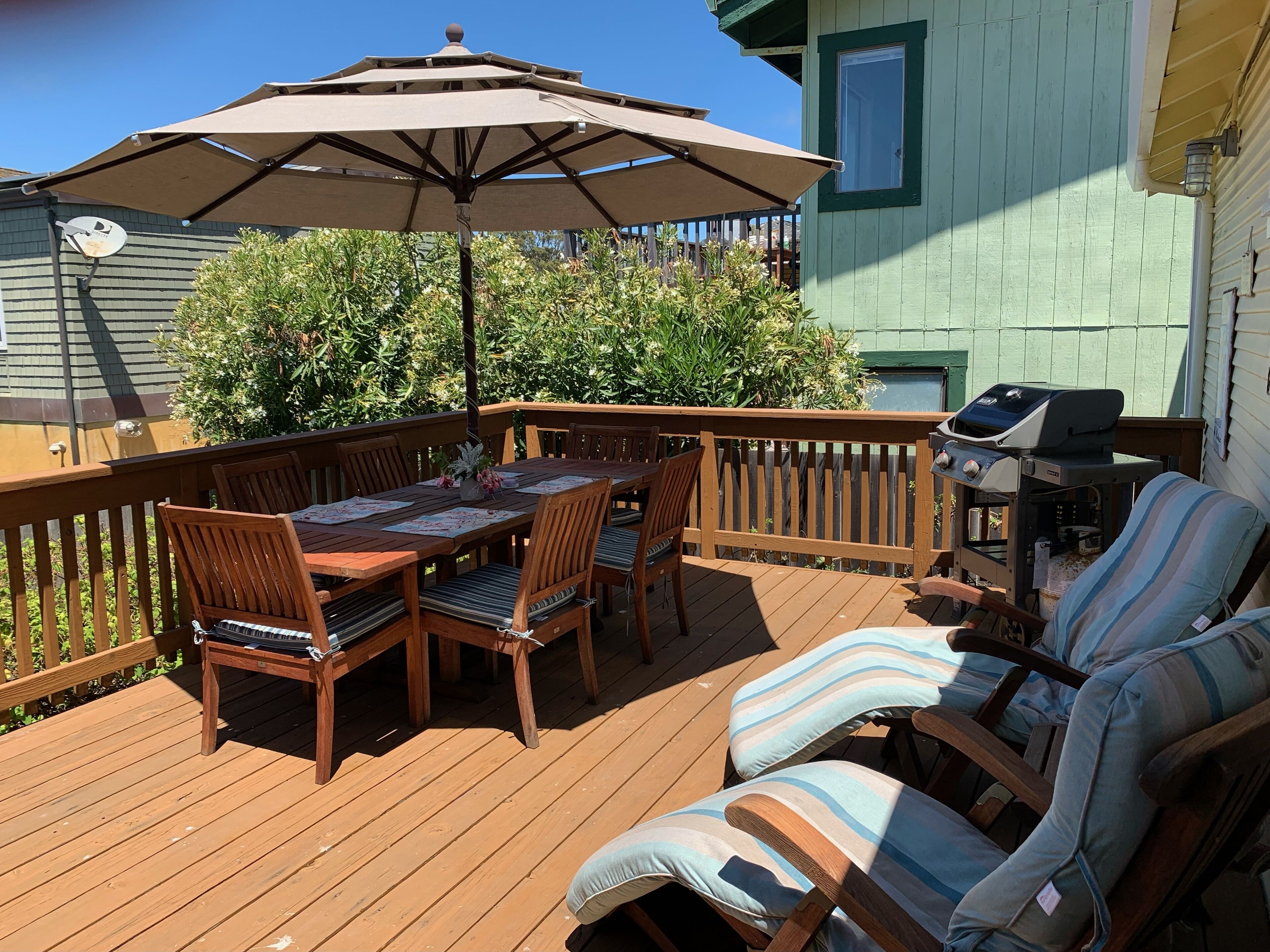 Eine Holzterrasse mit Tisch, Stühlen, einem Sonnenschirm und einem Grill.