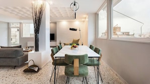 A modern dining area with a white table, green upholstered chairs, and a pendant light.