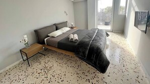 A modern bedroom with a bed, a small bedside table, a wall-mounted air conditioner, and a large window.