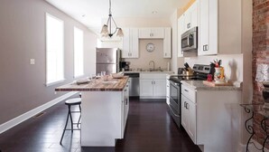 A modern kitchen with white cabinets, stainless steel appliances, and a large island with bar stools. - Charming 1BR Flat. The Hill/SW Gardens District (St. Louis)