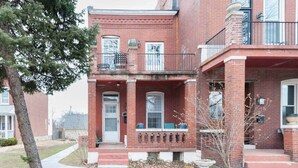 A two-story brick building with a front porch, a small balcony, and a visible front door. - Charming 1BR Flat. The Hill/SW Gardens District (St. Louis)