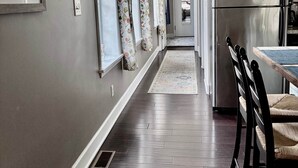 A modern kitchen with a stainless steel refrigerator, a dining area with a table and chairs, and a hallway with framed pictures on the wall. - Charming 1BR Flat. The Hill/SW Gardens District (St. Louis)
