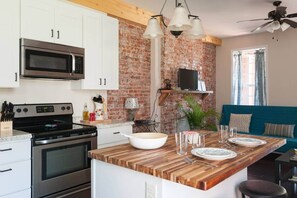 A kitchen with white cabinets, a brick wall, a wooden island, and a blue sofa in the living area.