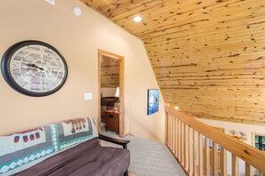 A cozy room with a wooden ceiling, a wall clock, a bench, and a staircase.