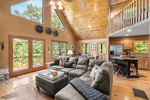 A spacious living room with a large sectional sofa, a dining area, and a kitchen with wooden cabinets.