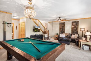 Een pooltafel in een kamer met een plafondventilator, een bank en een televisie.