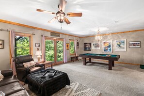 A room with a pool table, a leather chair, a ceiling fan, and artwork on the walls.